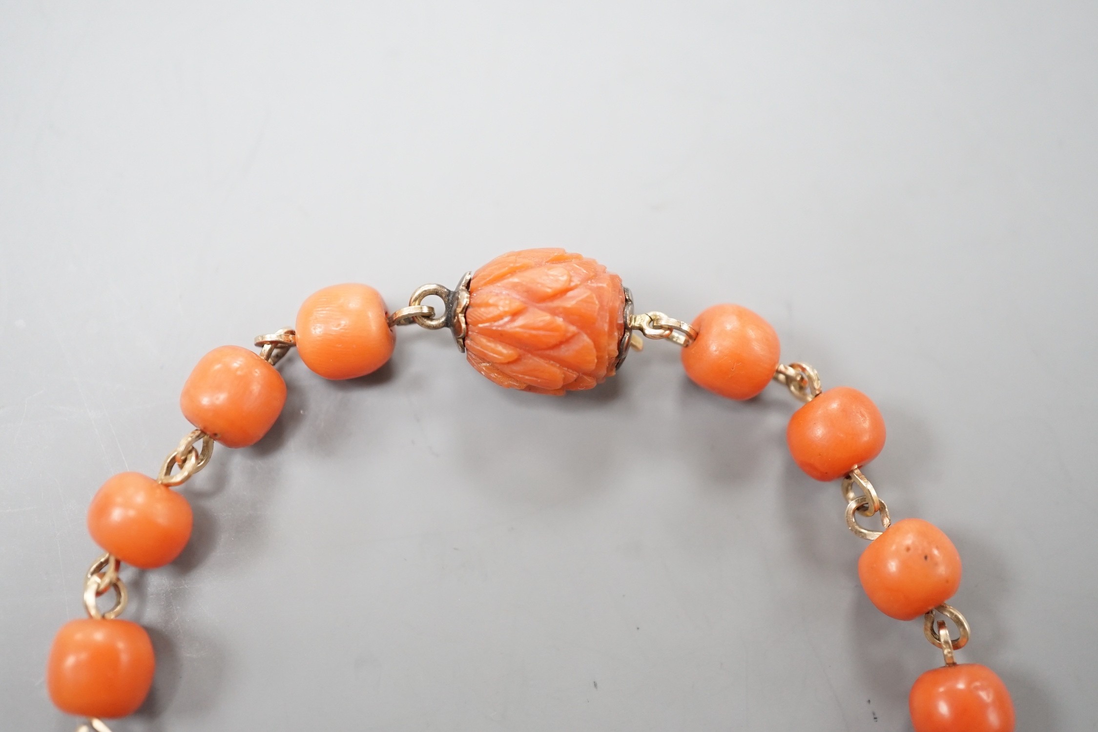 A yellow metal and coral bead bracelet, with carved coral bead clasp, 19.5cm.